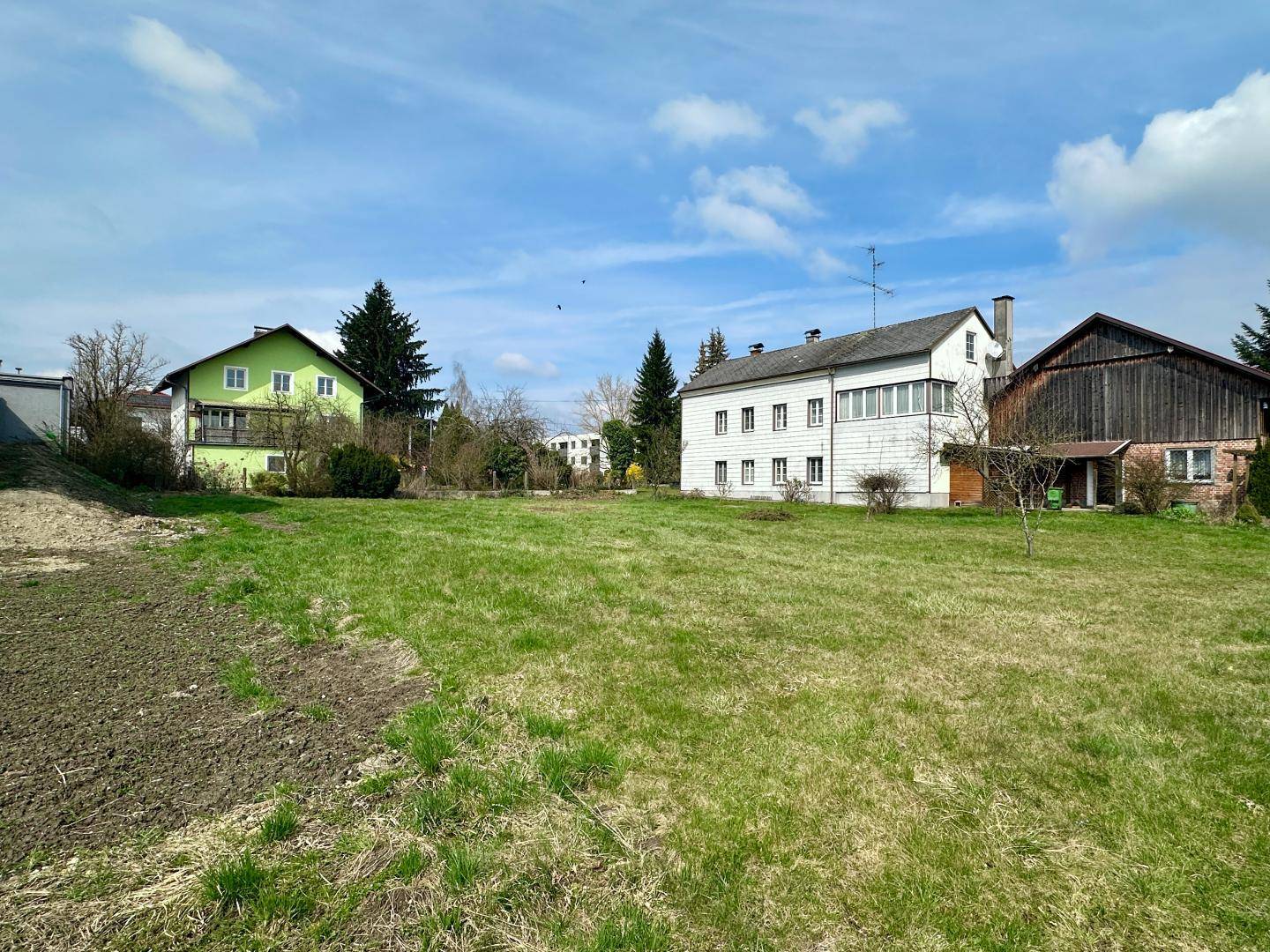 Weitläufige Rasenfläche vor einem traditionellen Haus mit Scheune und Nachbargebäuden.