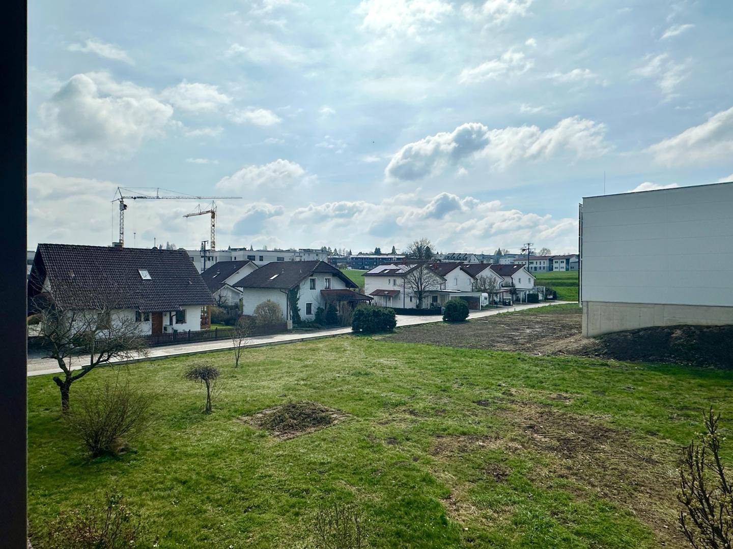 Blick aus dem Fenster auf eine Wohnsiedlung mit Häusern und Baukranen am Horizont.