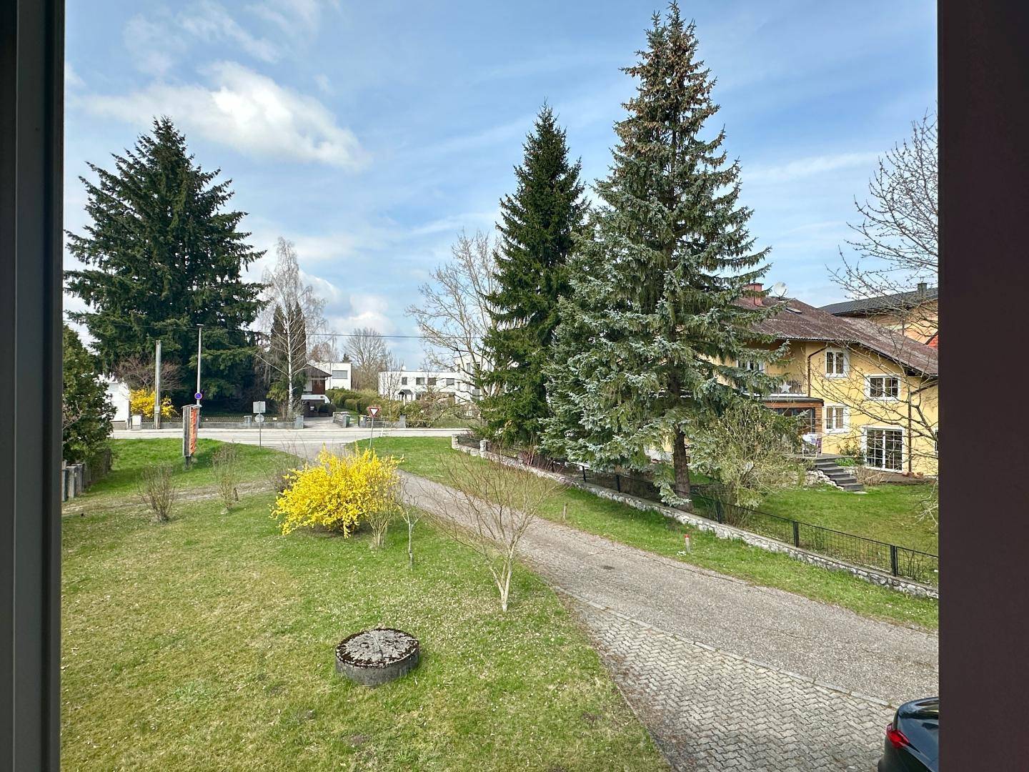 Weitläufiger Blick aus dem Fenster auf eine grüne Umgebung mit Bäumen und Häusern.
