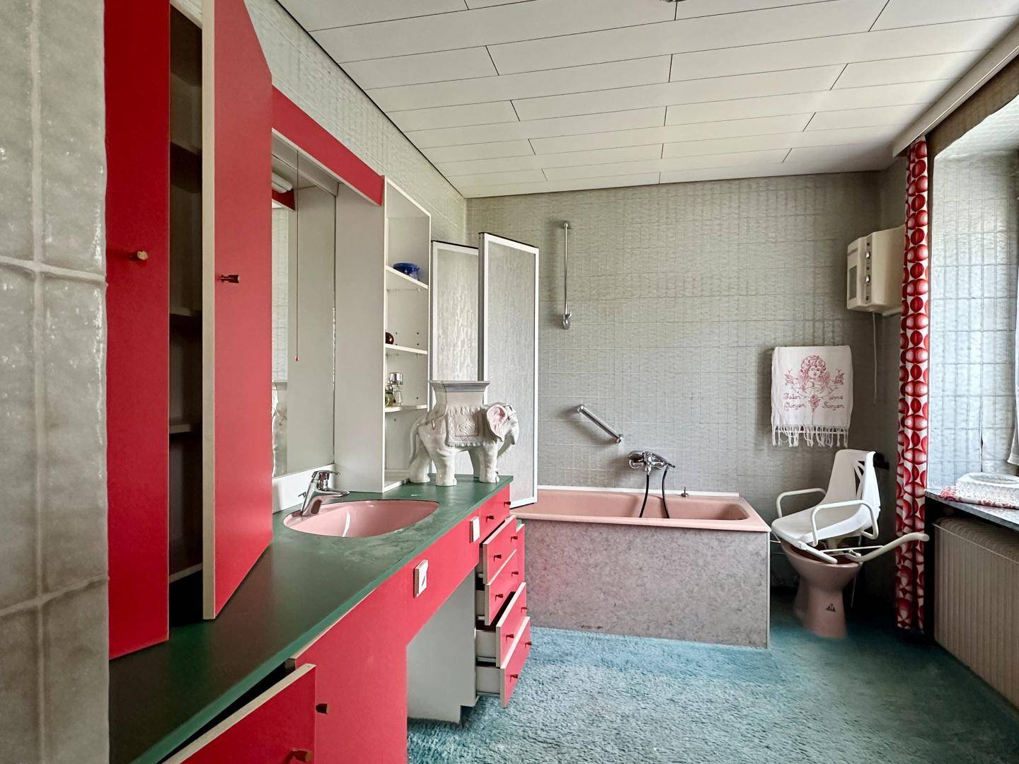Badezimmer im 80er-Jahre-Stil mit rosa Badewanne, Waschbecken und bunten Schränken.