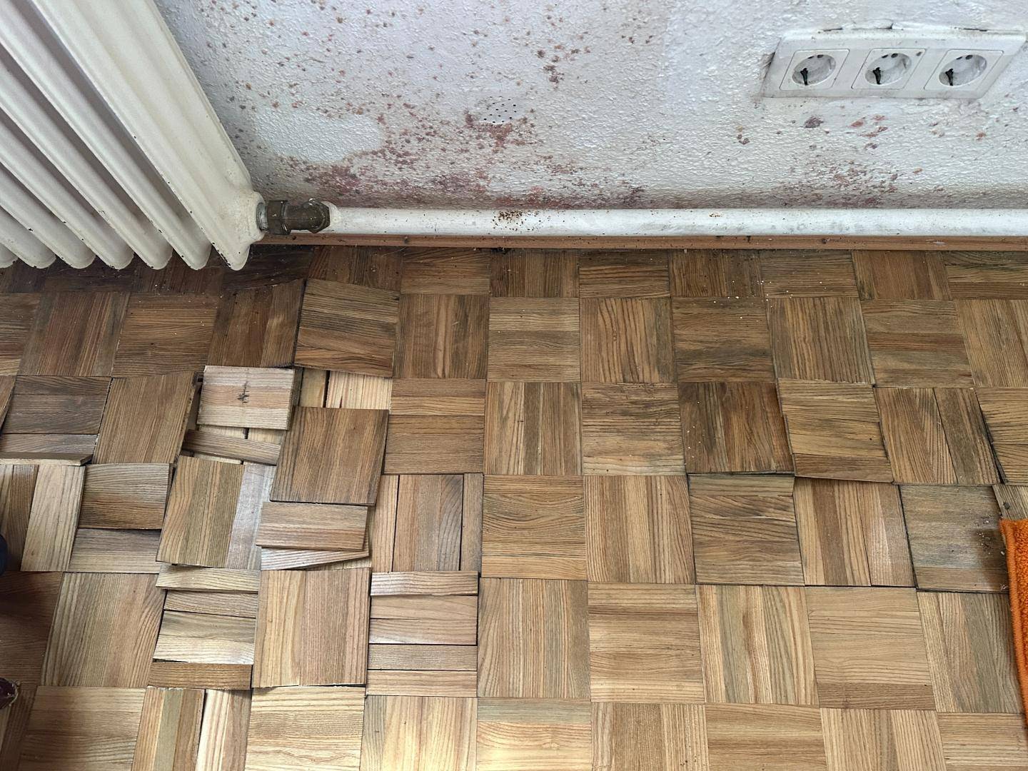 Beschädigter Parkettboden mit losen Holzstücken, der dringend renoviert werden muss.