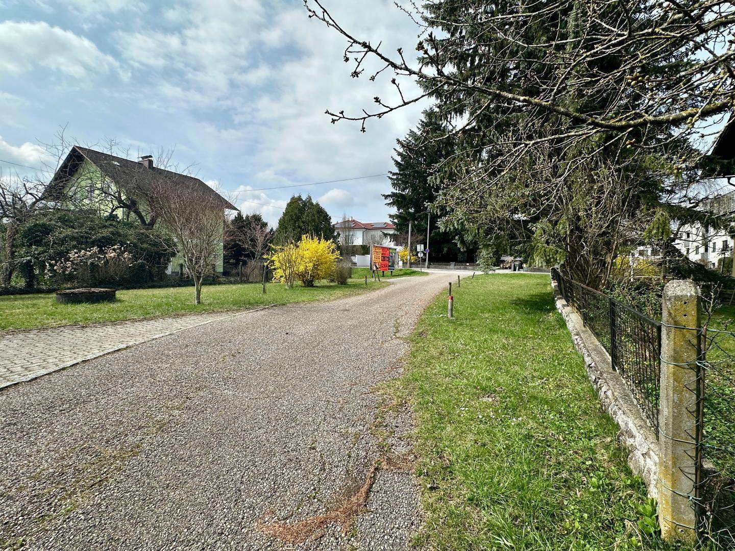 Kiesauffahrt umgeben von Grünflächen und Bäumen, führt zu einer Straße.