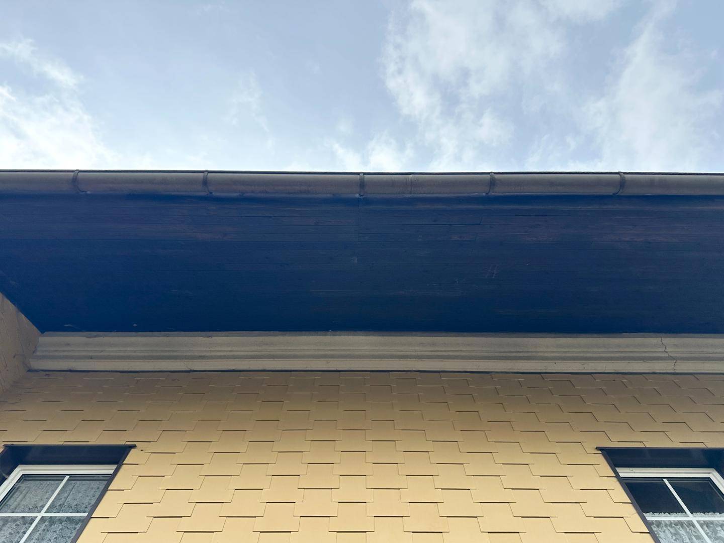 Detailansicht der Fassade mit Dachüberstand und Fenstern unter bewölktem Himmel.