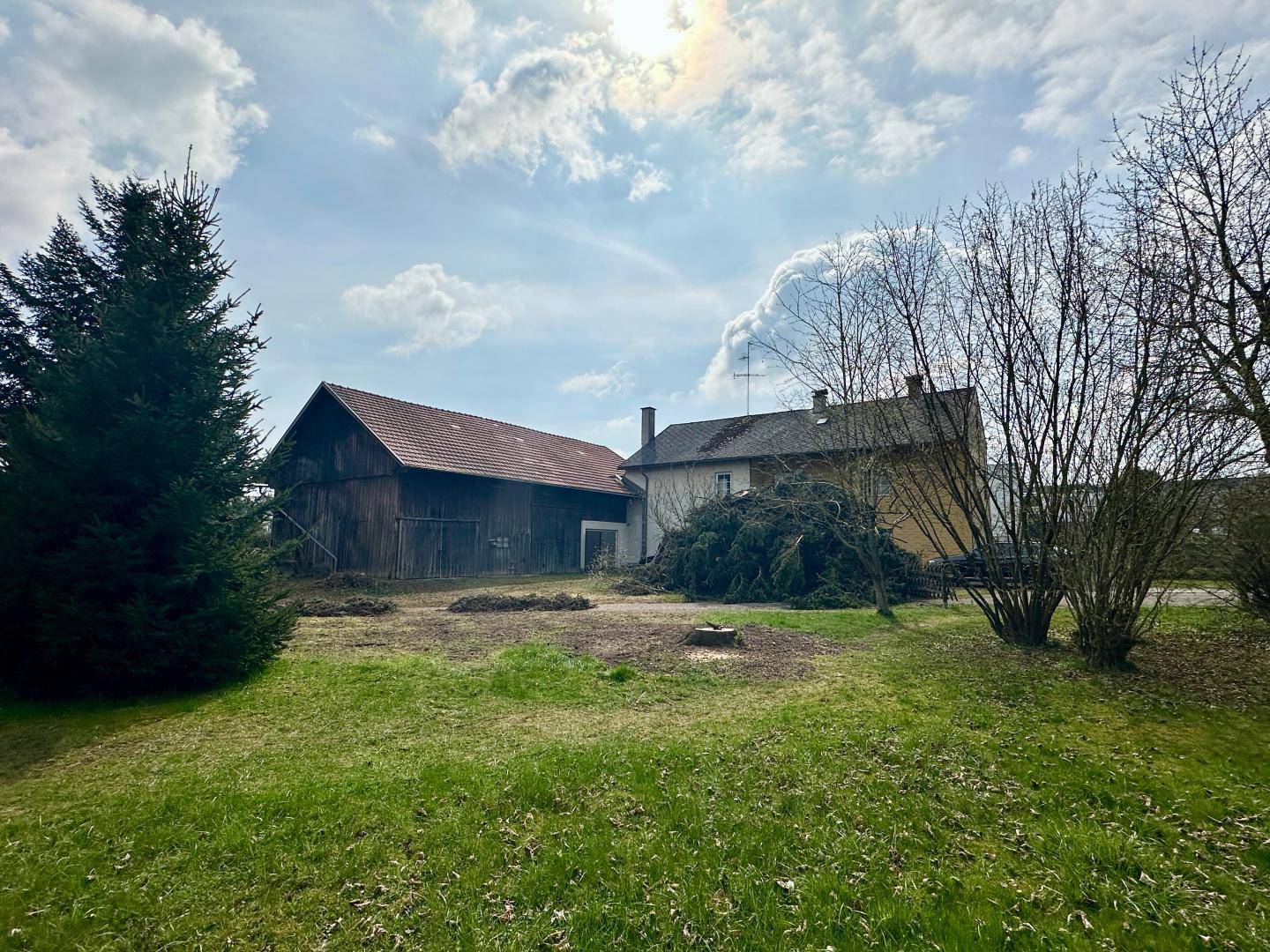 Weitläufiges Grundstück mit Haus und Scheune unter einem sonnigen, bewölkten Himmel.