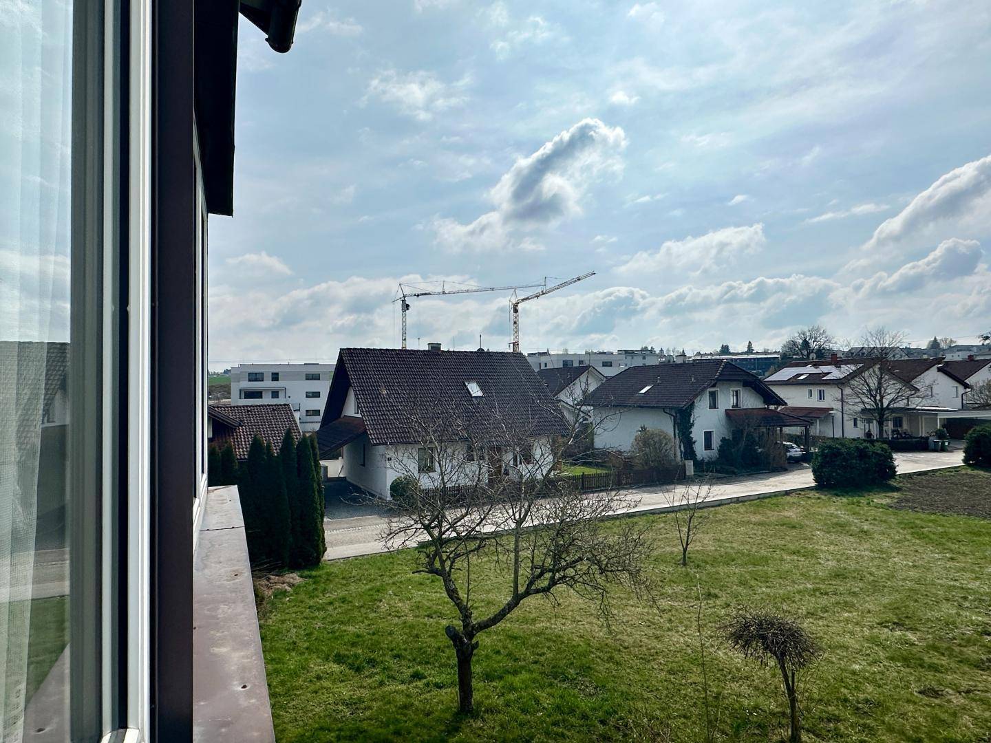 Weitblick aus dem Fenster auf eine Wohnsiedlung mit Baukranen am Horizont.