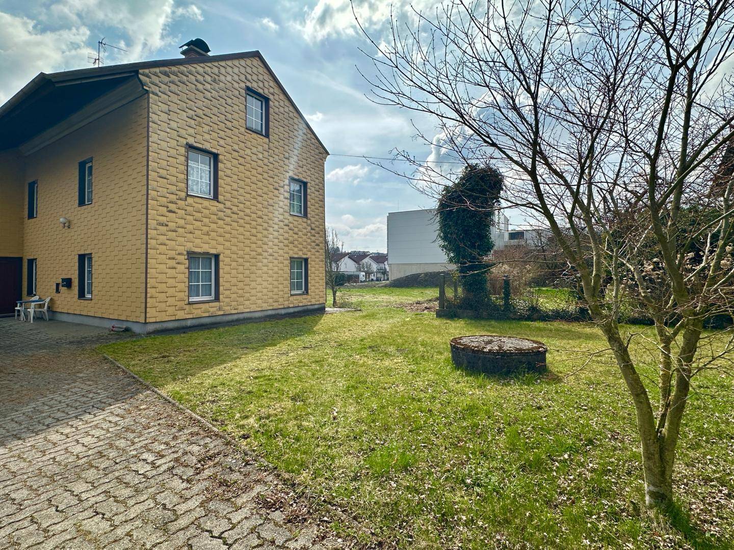 Gelbe Fassade eines Hauses mit gepflastertem Bereich und Rasenfläche im Vordergrund.
