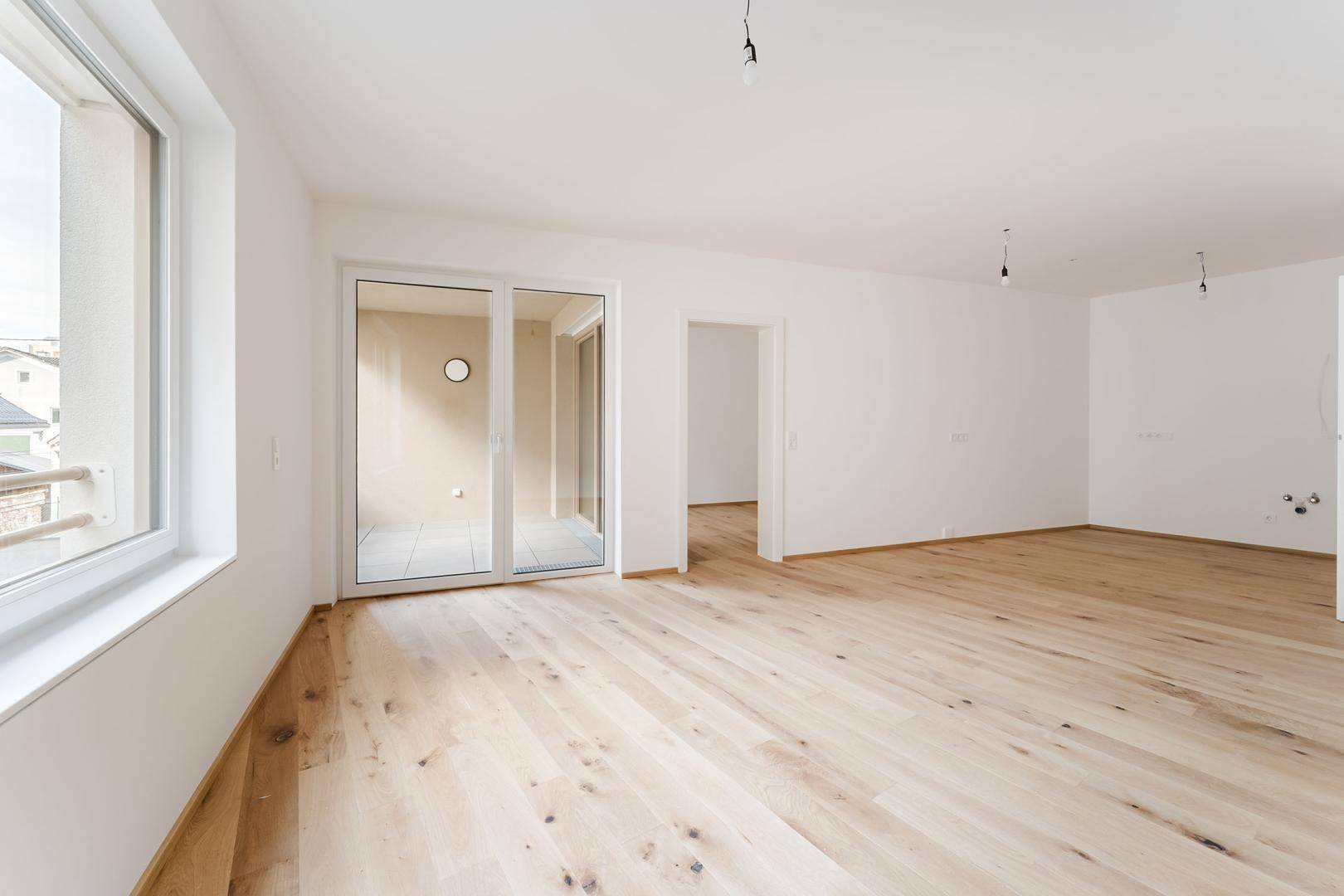 Geräumiges, helles Zimmer mit Holzboden und Schiebetür zum Balkon, bereit für individuelle Gestaltung.