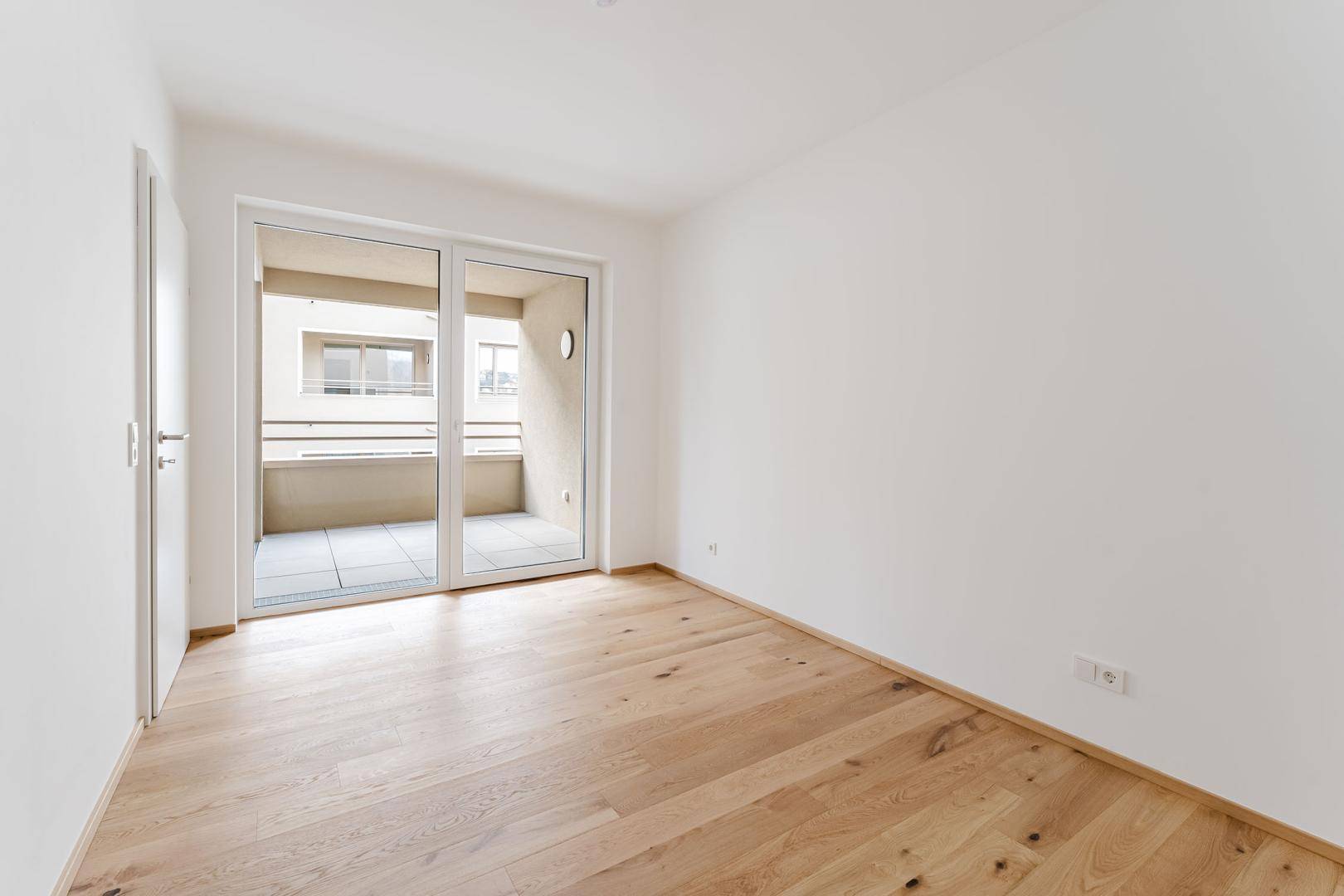 Ruhiges Schlafzimmer mit hellem Holzboden und direktem Zugang zu einem privaten Balkon.