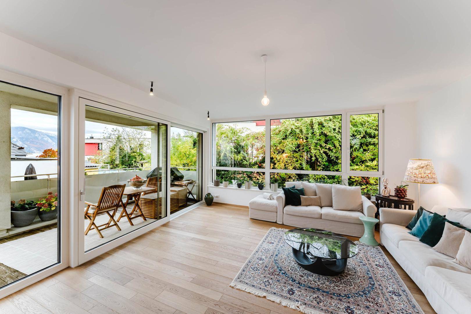 Helles Wohnzimmer mit großen Fensterfronten, Parkettboden und Zugang zum Balkon.