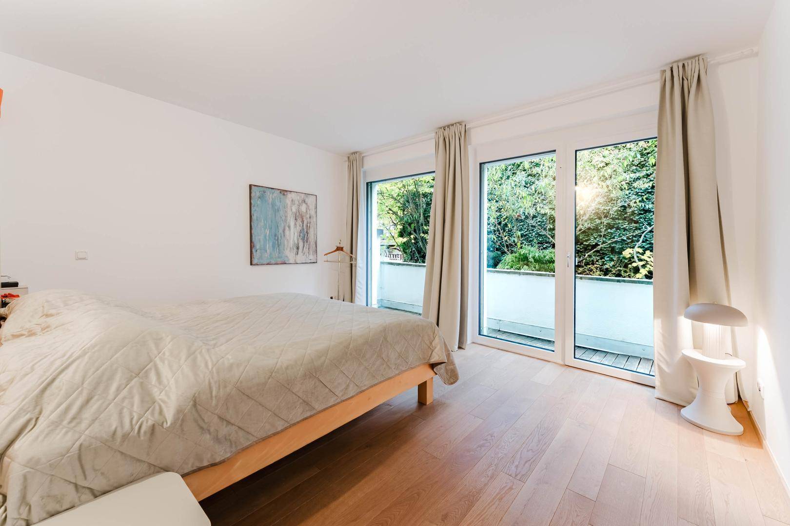 Schlafzimmer mit Holzbett, Parkettboden und großen Fenstern mit Blick ins Grüne.