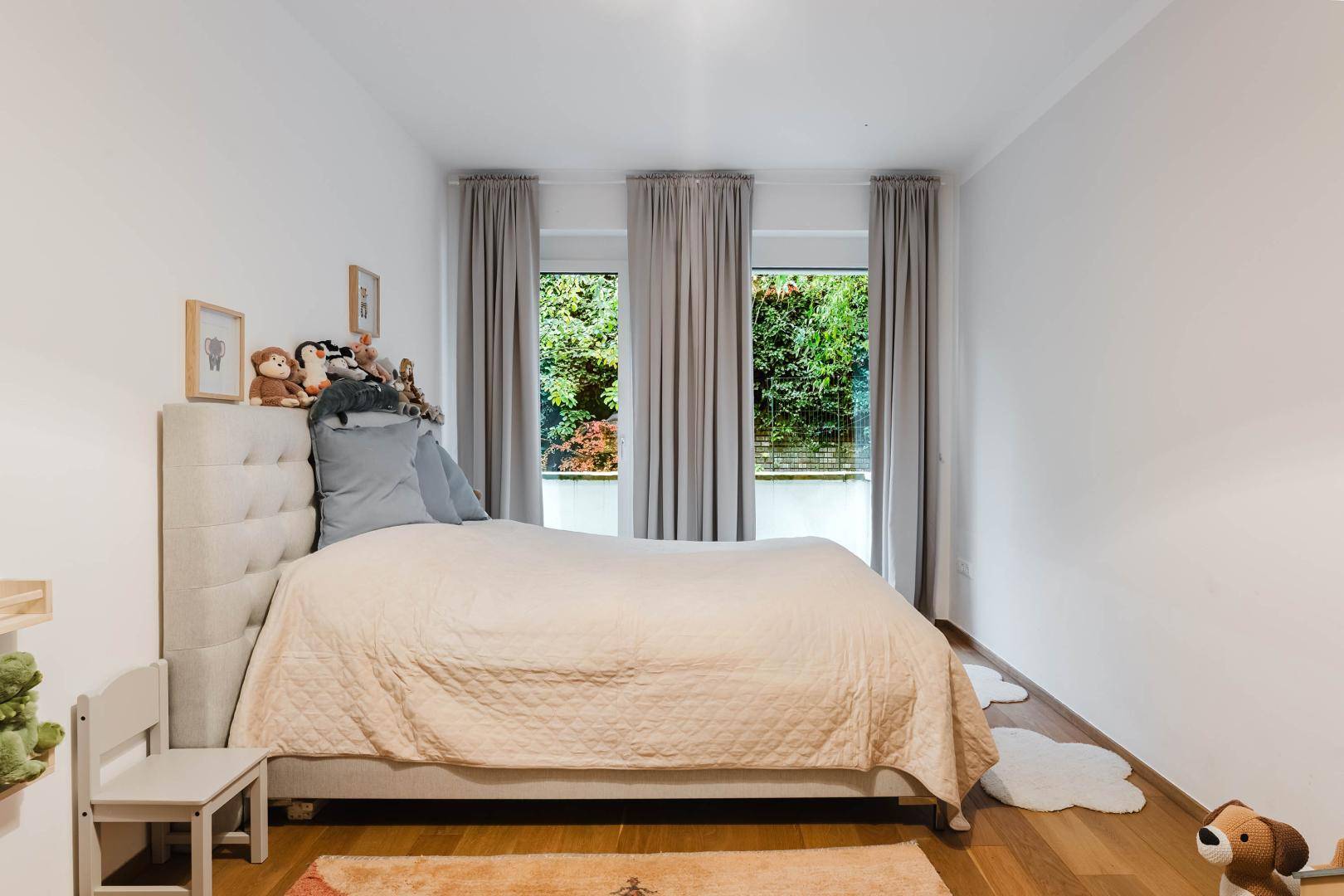 Gemütliches Schlafzimmer mit Parkettboden und Blick ins Grüne durch die Fenster.