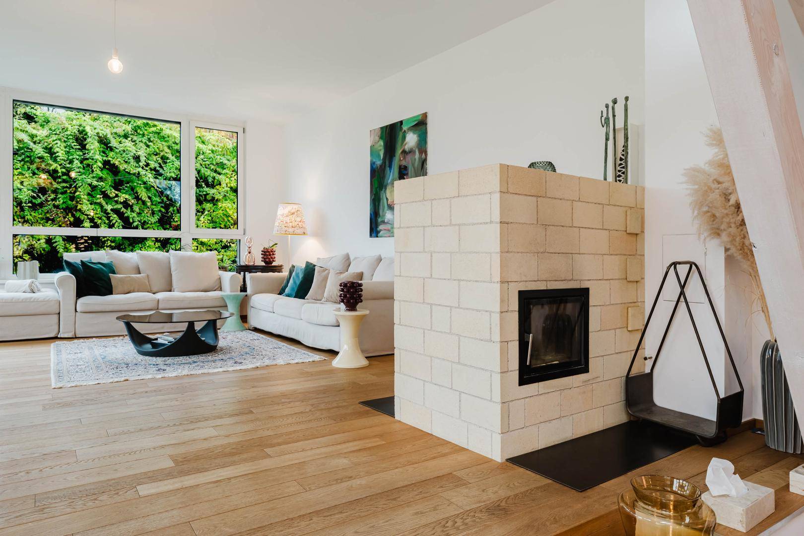 Helles Wohnzimmer mit Kamin, großen Fenstern und Blick ins Grüne.