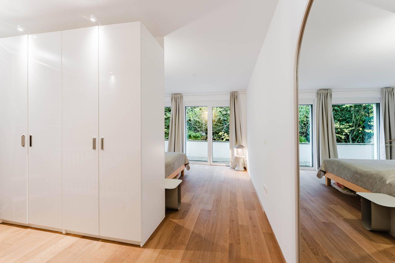 Helles Schlafzimmer mit weißen Schränken, Parkettboden und Zugang zum Balkon.