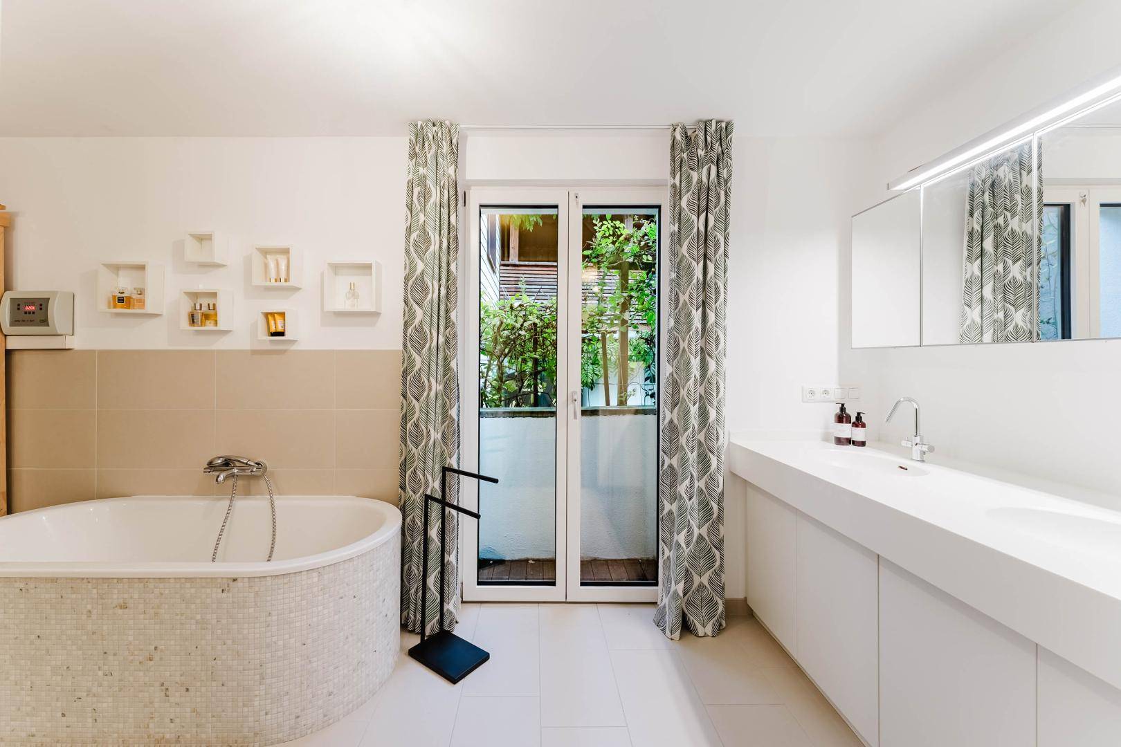 Modernes Badezimmer mit Badewanne, Doppelwaschbecken und Zugang zum Balkon.