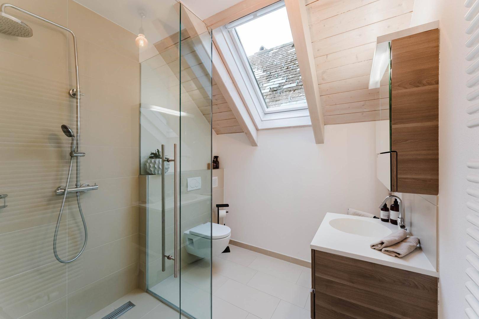 Helles Badezimmer im Dachgeschoss mit Dusche, WC und Dachfenster.
