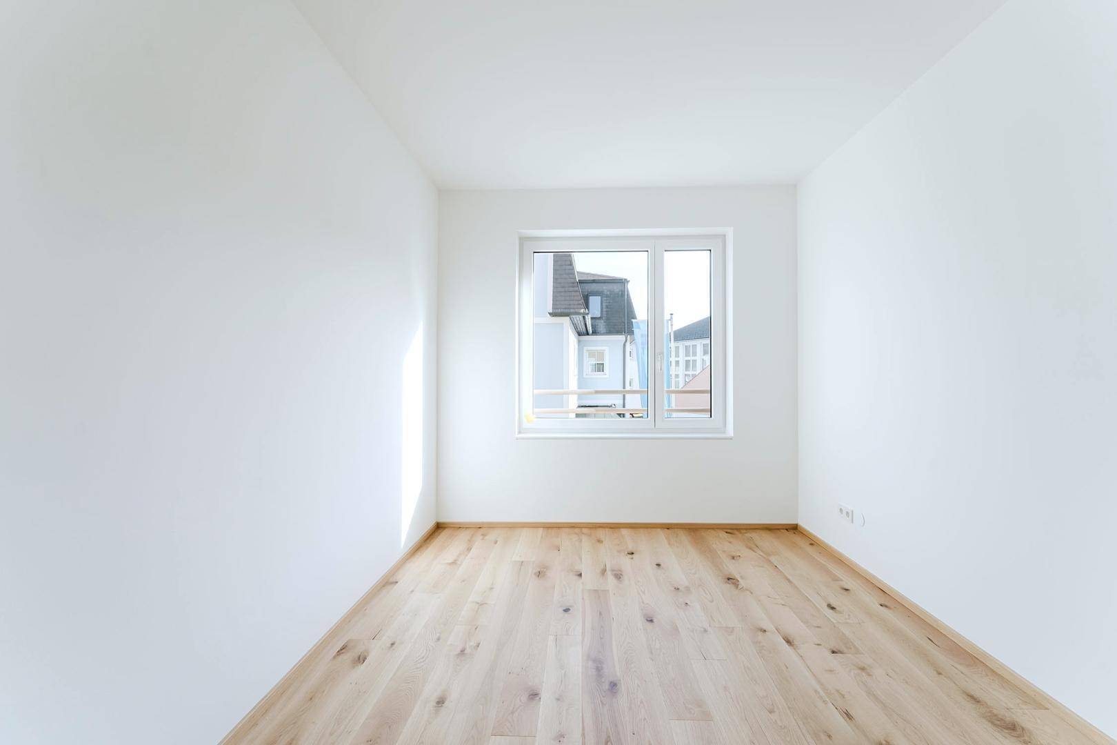 Leeres Schlafzimmer mit hellem Holzboden und einem Fenster, das den Blick nach draußen freigibt.