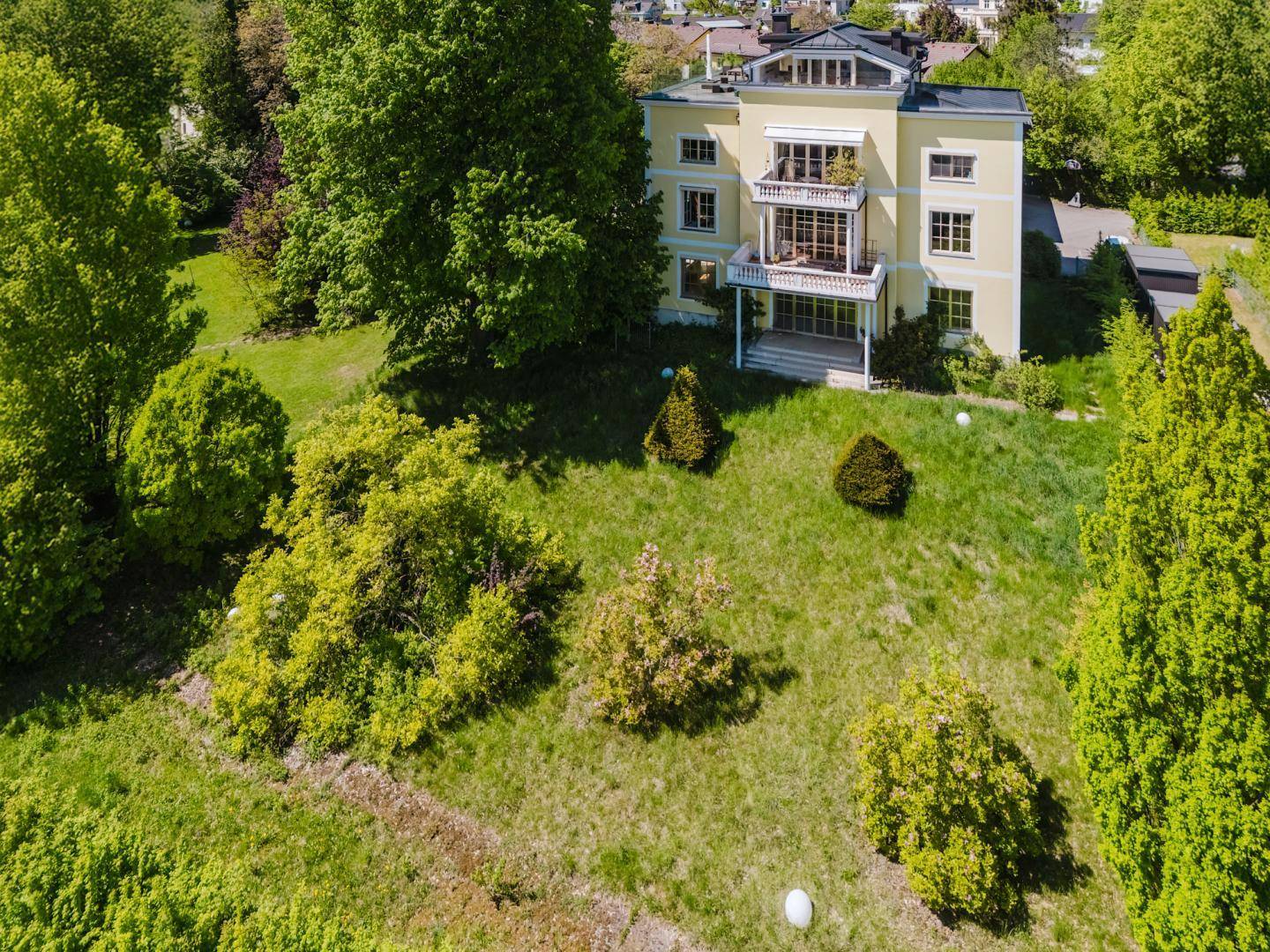 Hochwinkel-Luftaufnahme der gelben Villa, die das gesamte Anwesen mit seinem großen Garten zeigt.