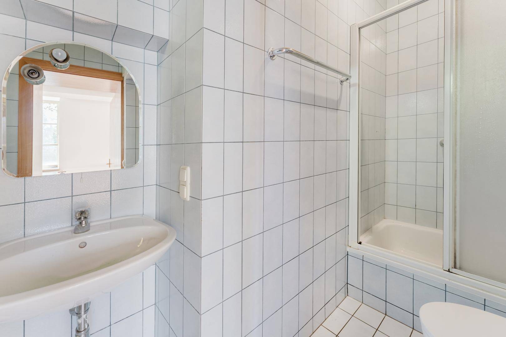 Funktionales Badezimmer mit weißen Fliesen, einem Waschbecken und einer Duschkabine.