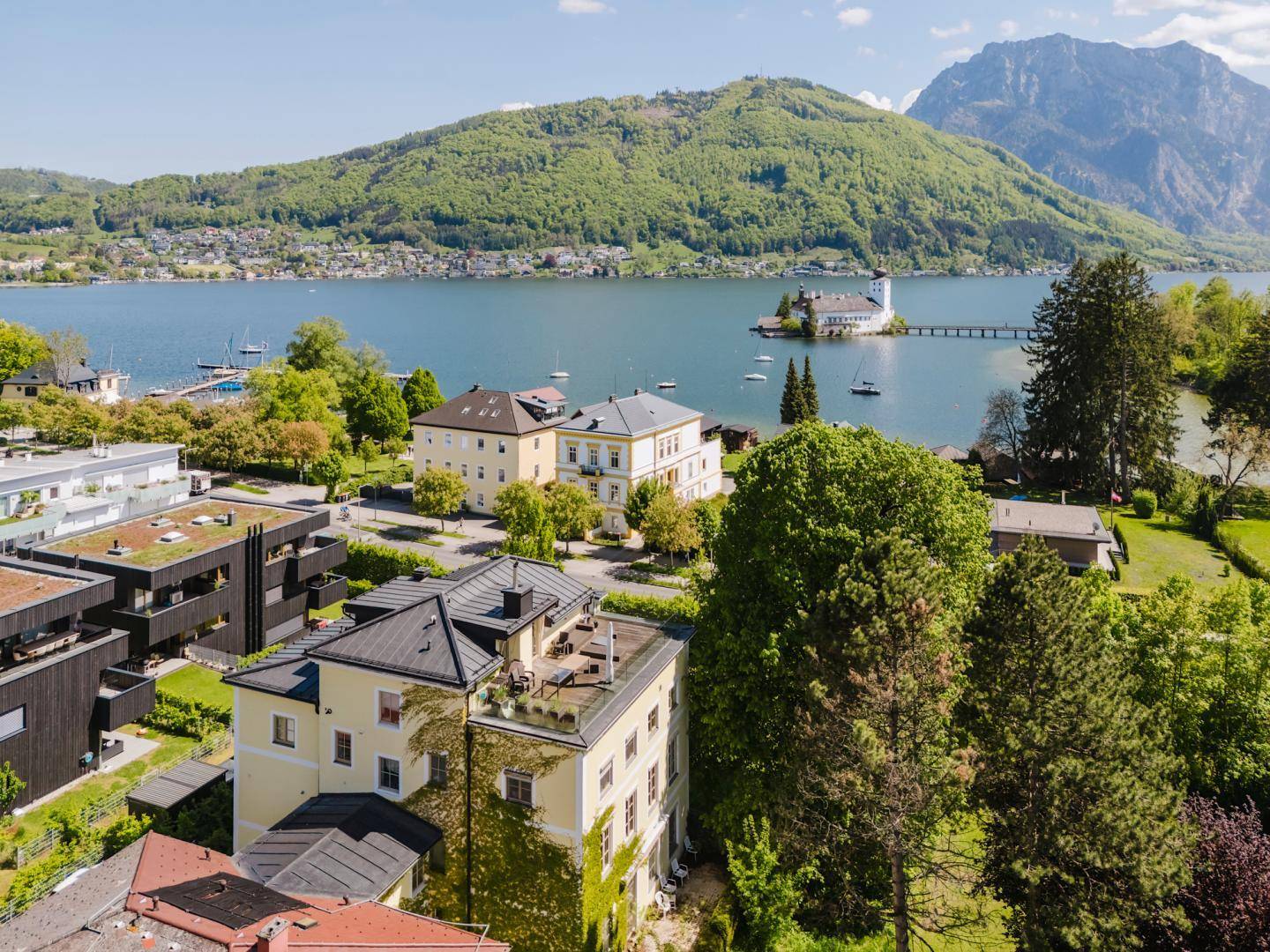 Panoramablick aus der Luft auf den See, die Berge und die umliegende Bebauung mit viel Grün.