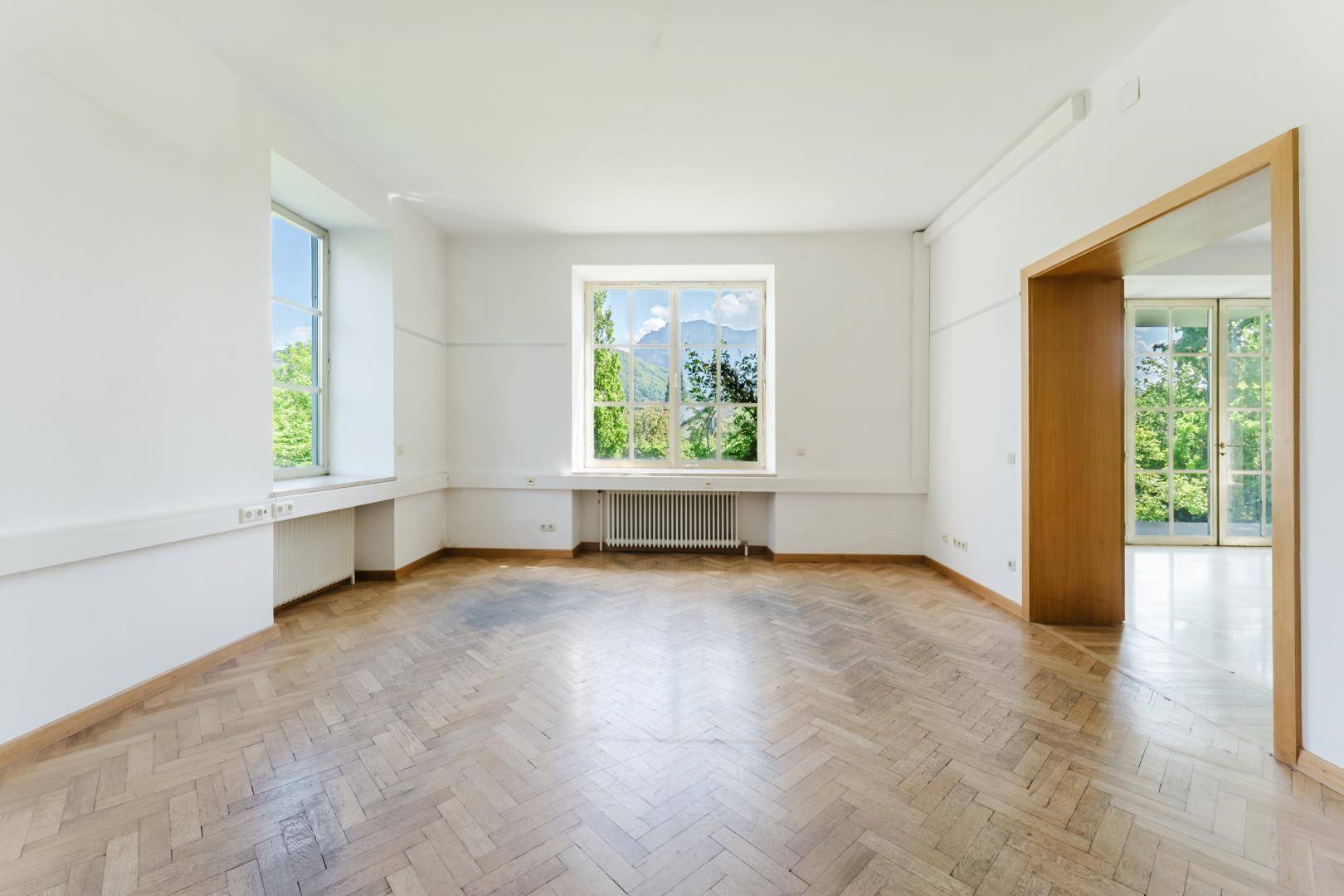 Geräumiger Raum mit klassischem Fischgrätparkett und mehreren Fenstern, die einen schönen Bergblick bieten.