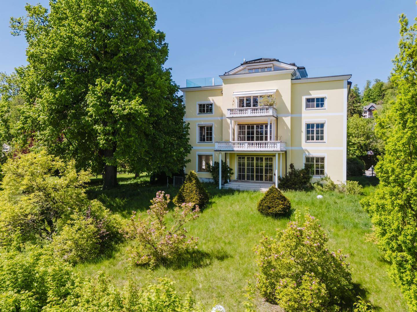 Panoramablick aus der Luft auf die elegante gelbe Villa und ihren weitläufigen, grünen Park.