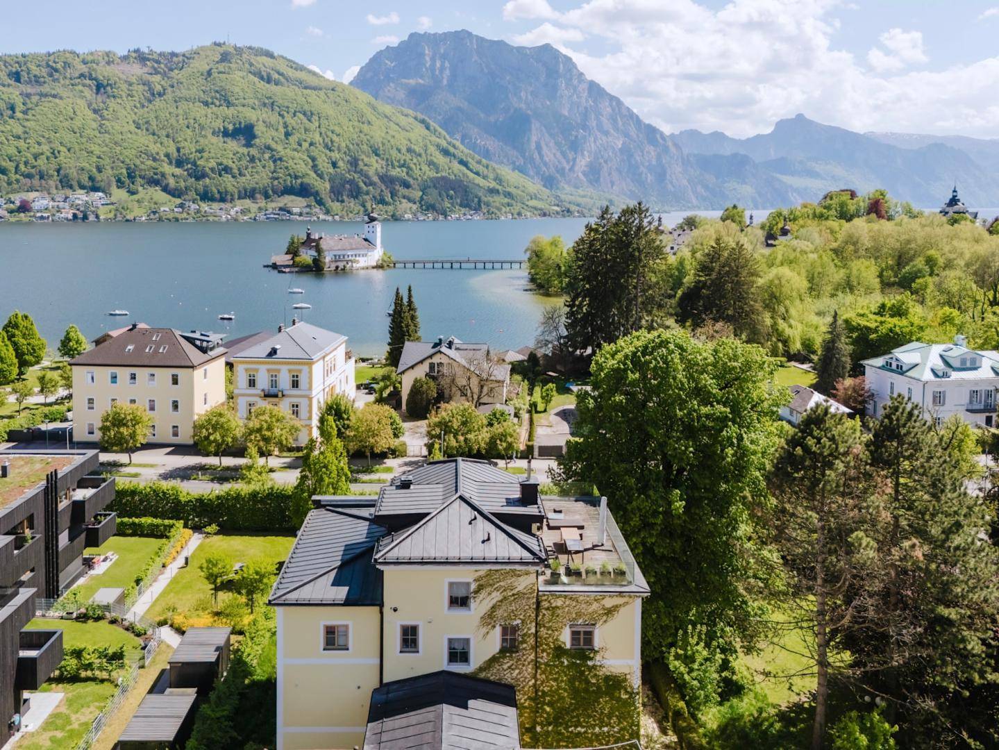Luftaufnahme mit malerischem Blick auf den See, die Berge und die umliegende Wohnbebauung.