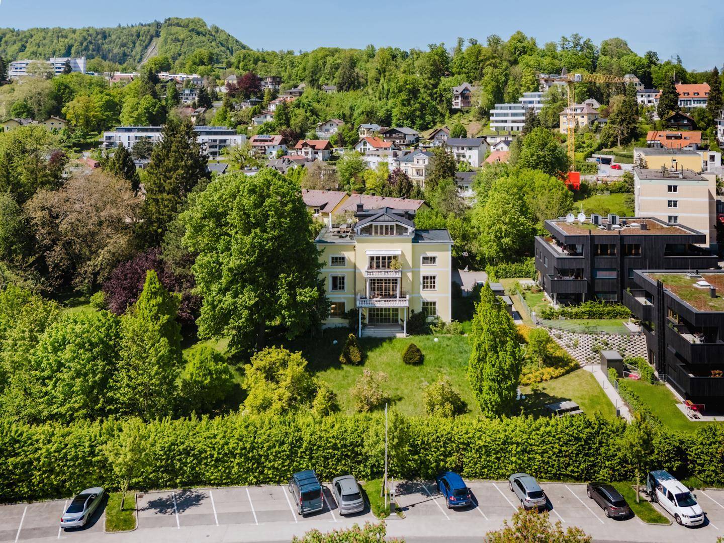 Luftaufnahme der Villa und ihrer Umgebung, einschließlich eines Parkplatzes und weiterer Wohngebäude.
