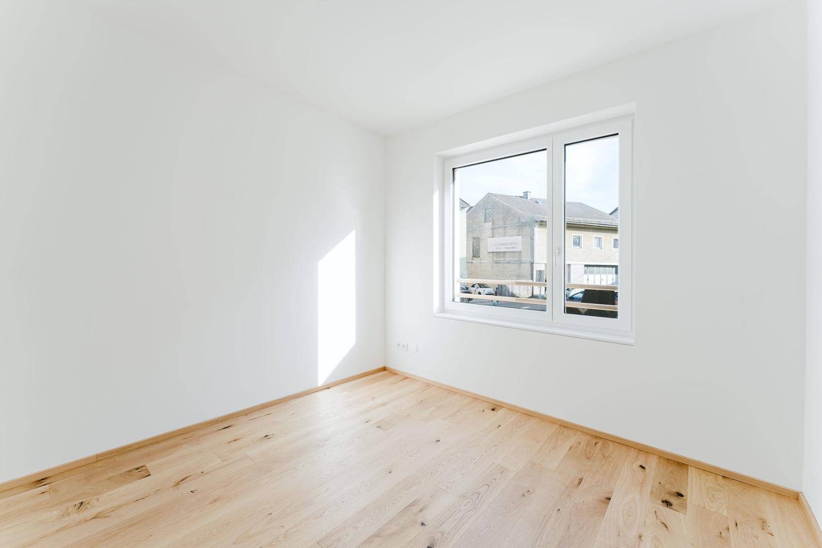 Helles Schlafzimmer mit Holzboden und großem Fenster, das viel Tageslicht hereinlässt.