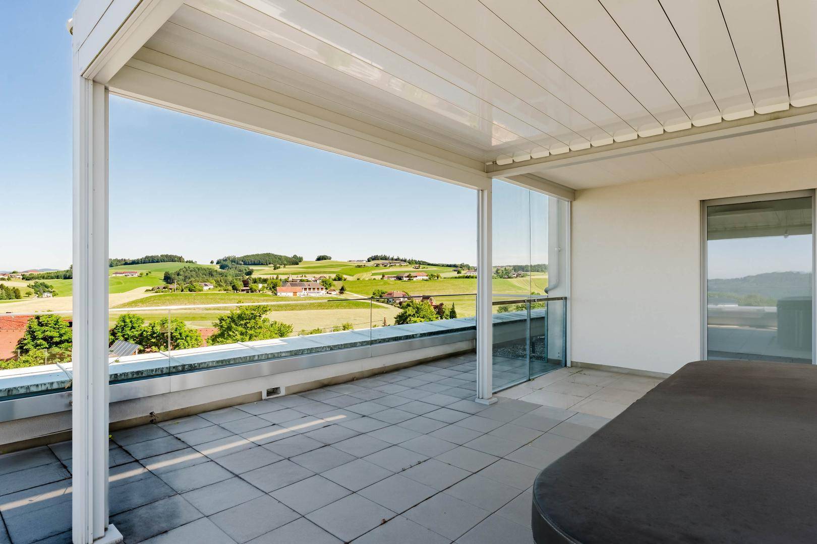 Helle Dachterrasse mit Glasgeländer und weitem Blick über die hügelige Landschaft.