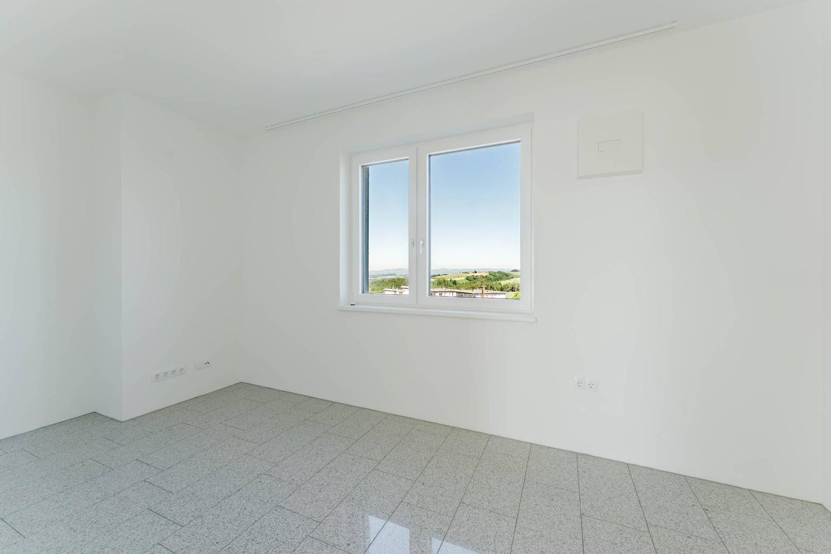 Heller Raum mit Fliesenboden und Fenster mit Blick auf die grüne Landschaft.