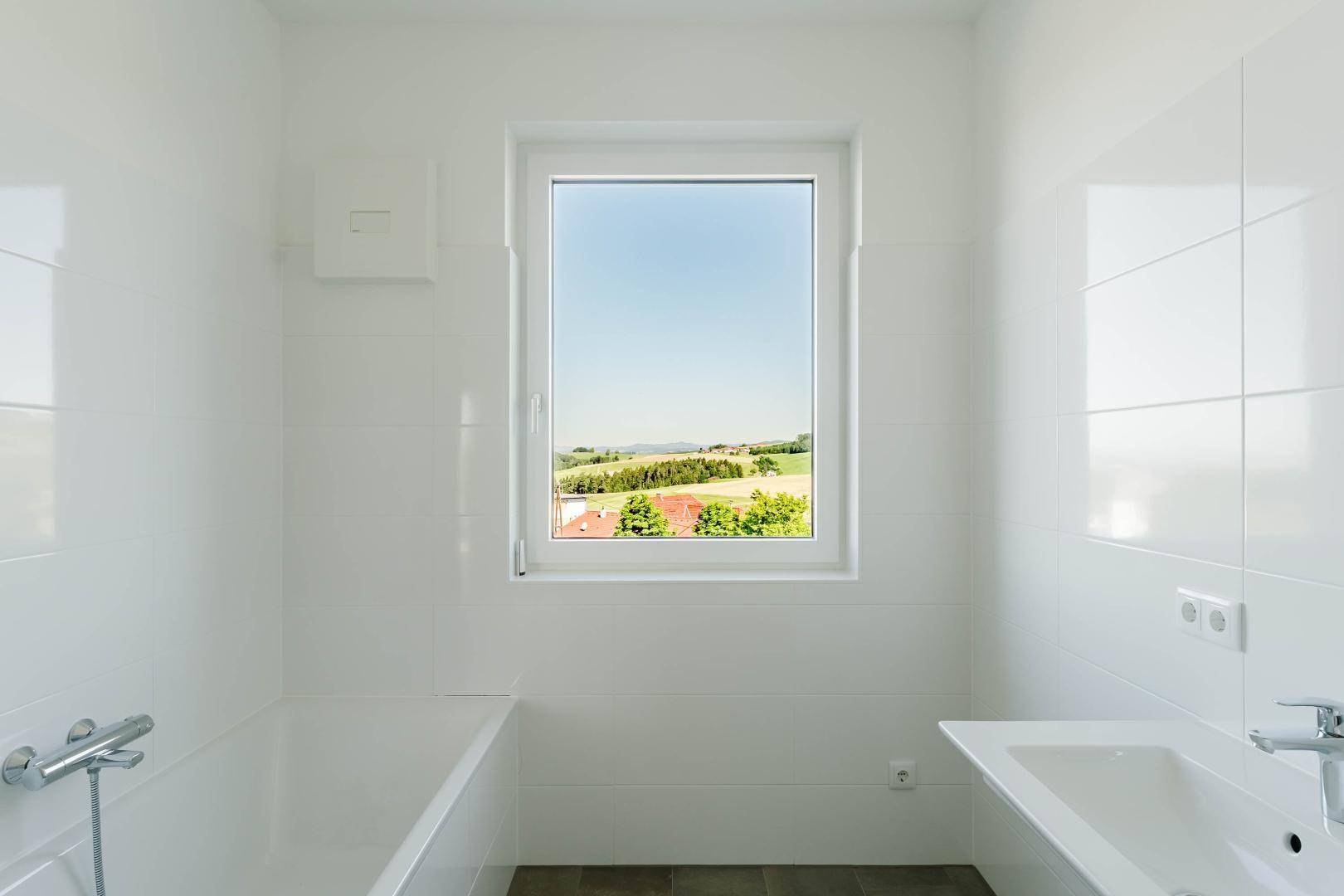 Detailansicht des Badezimmers mit Badewanne und einem Fenster, das einen weiten Blick ins Grüne freigibt.