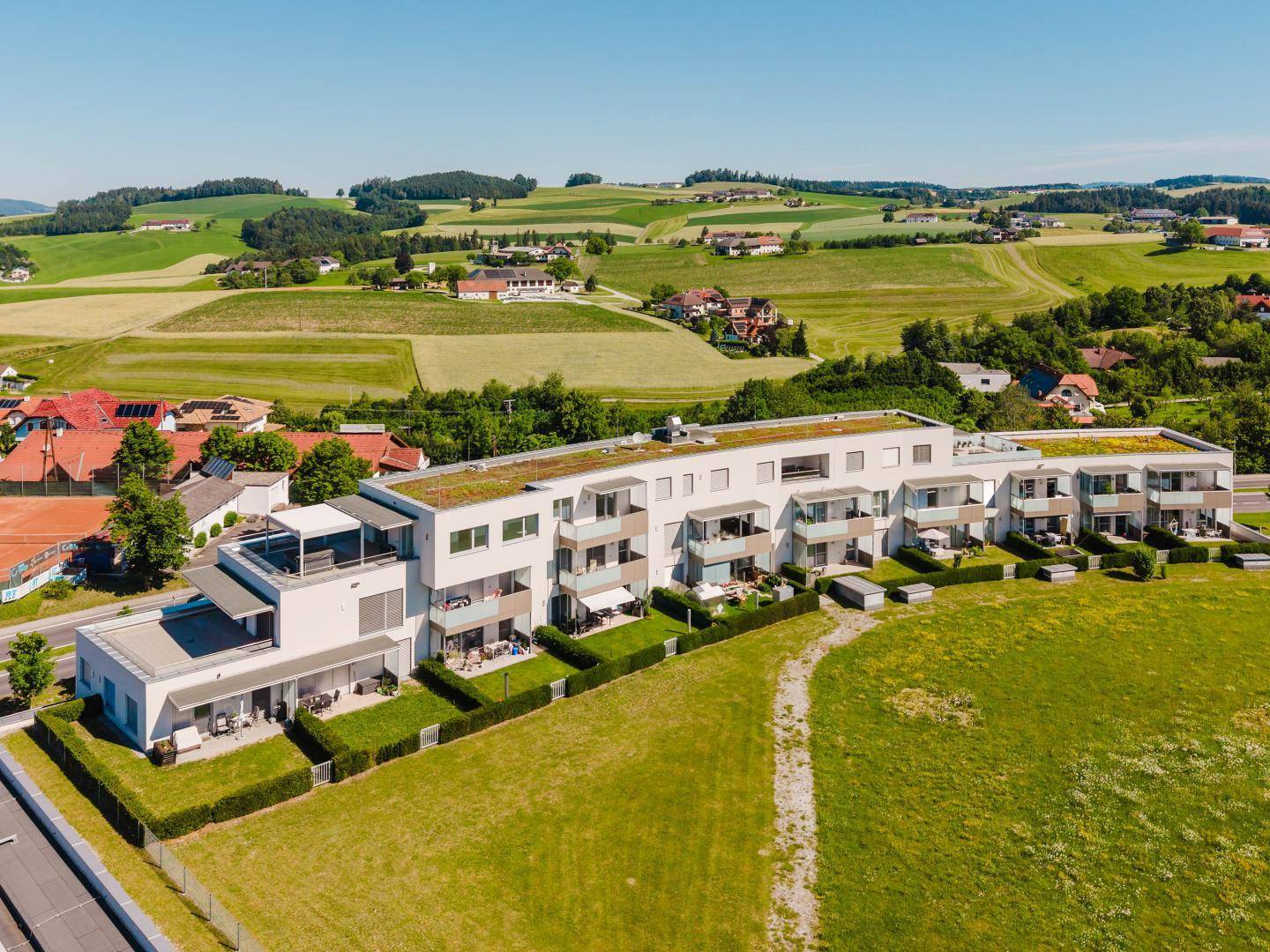 Moderner Wohnkomplex mit Balkonen, Gärten und Gründächern in ländlicher Umgebung.