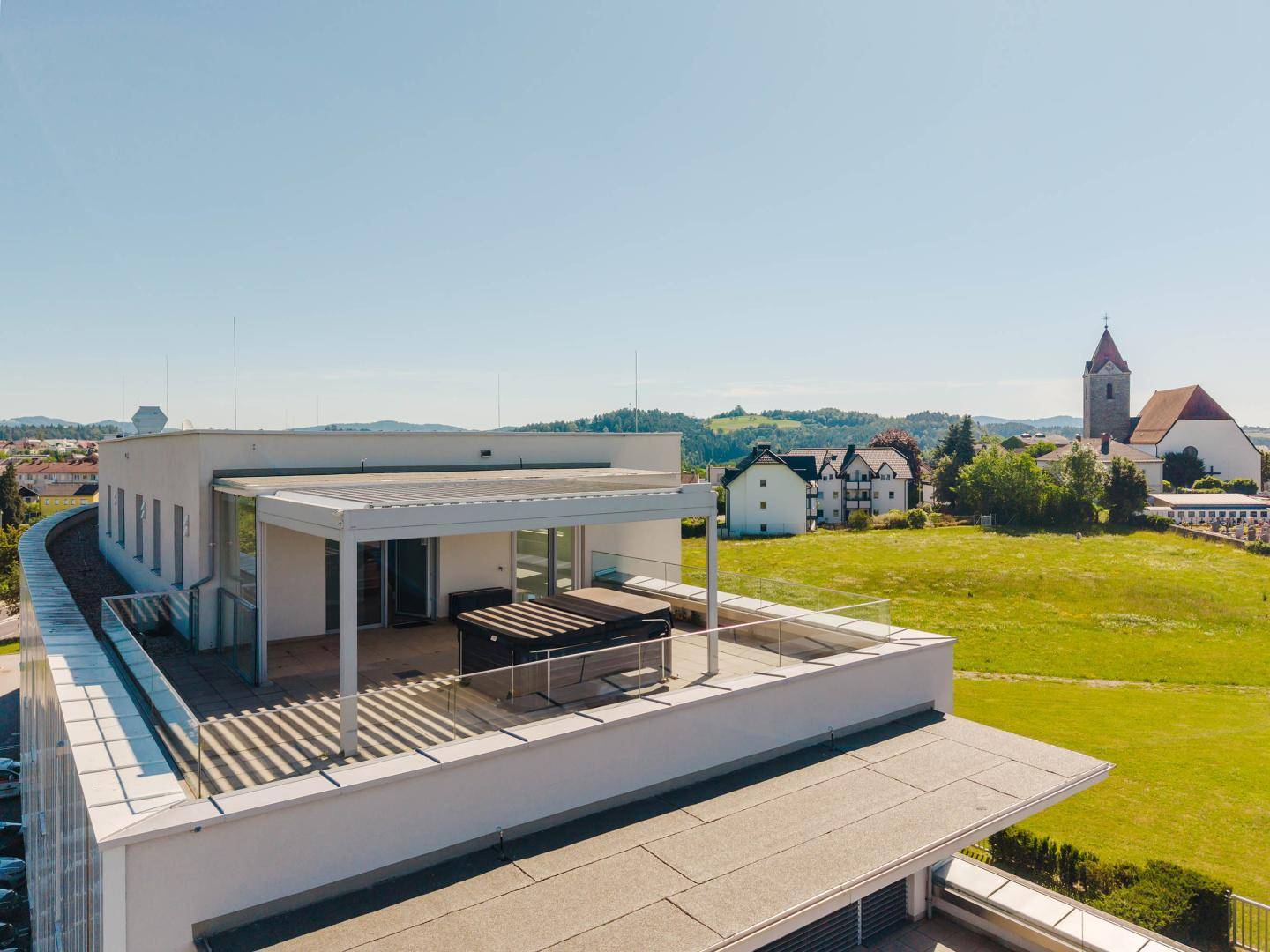 Weitläufige Dachterrasse mit Whirlpool und Glasgeländer, umgeben von grüner Landschaft.