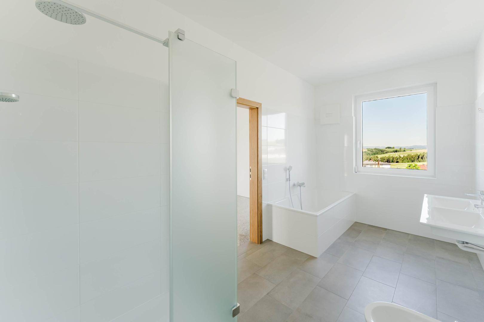 Helles Badezimmer mit Dusche, Badewanne und Fenster, das einen schönen Ausblick auf die Landschaft bietet.