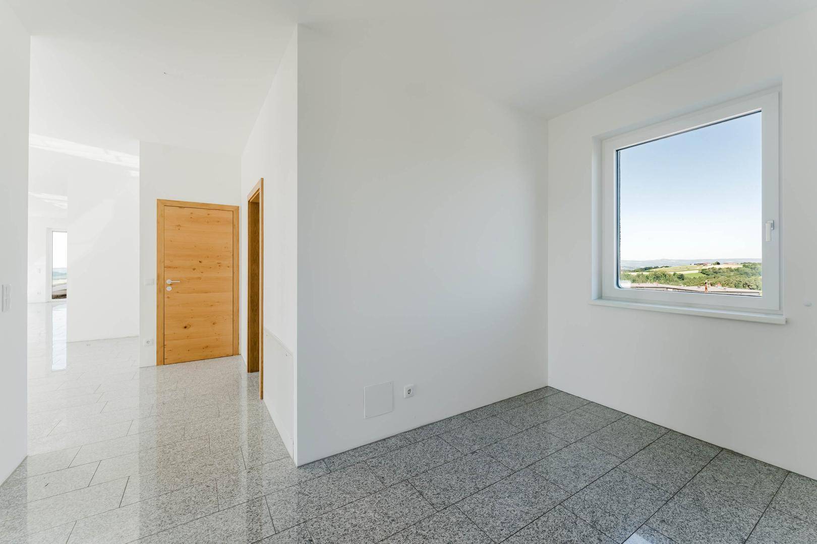 Leeres Zimmer mit Holztür und Fenster, das einen ruhigen Blick auf die grüne Umgebung bietet.