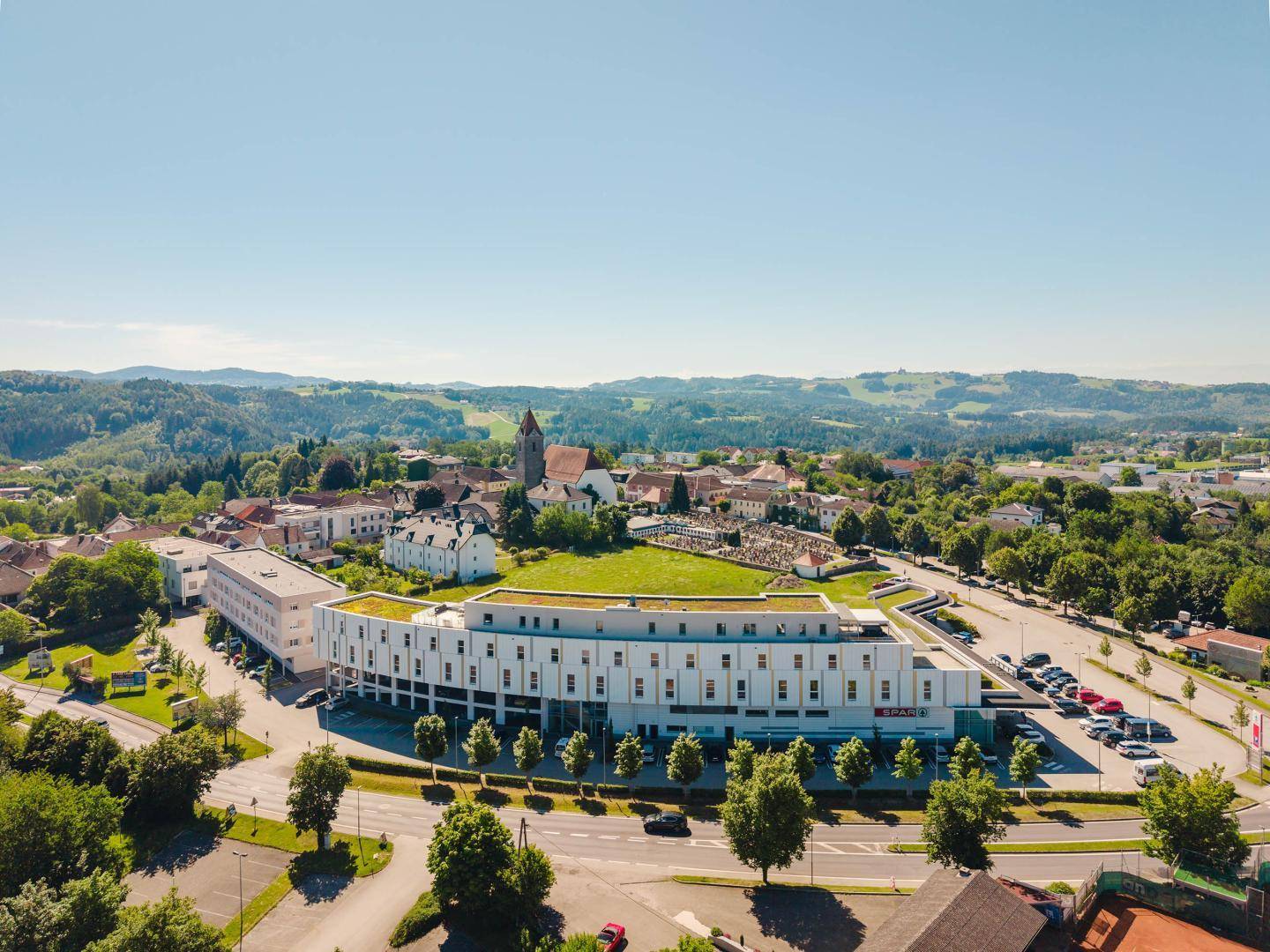 Weitläufige Luftaufnahme des modernen Gebäudes und der umliegenden Stadt mit viel Grün.