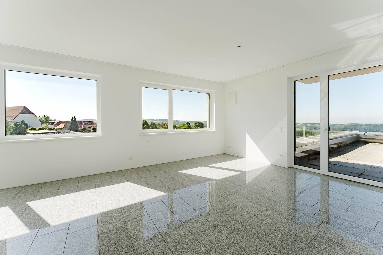 Heller Wohnraum mit großen Fenstern und Schiebetür, die Zugang zu einer weitläufigen Terrasse bietet.