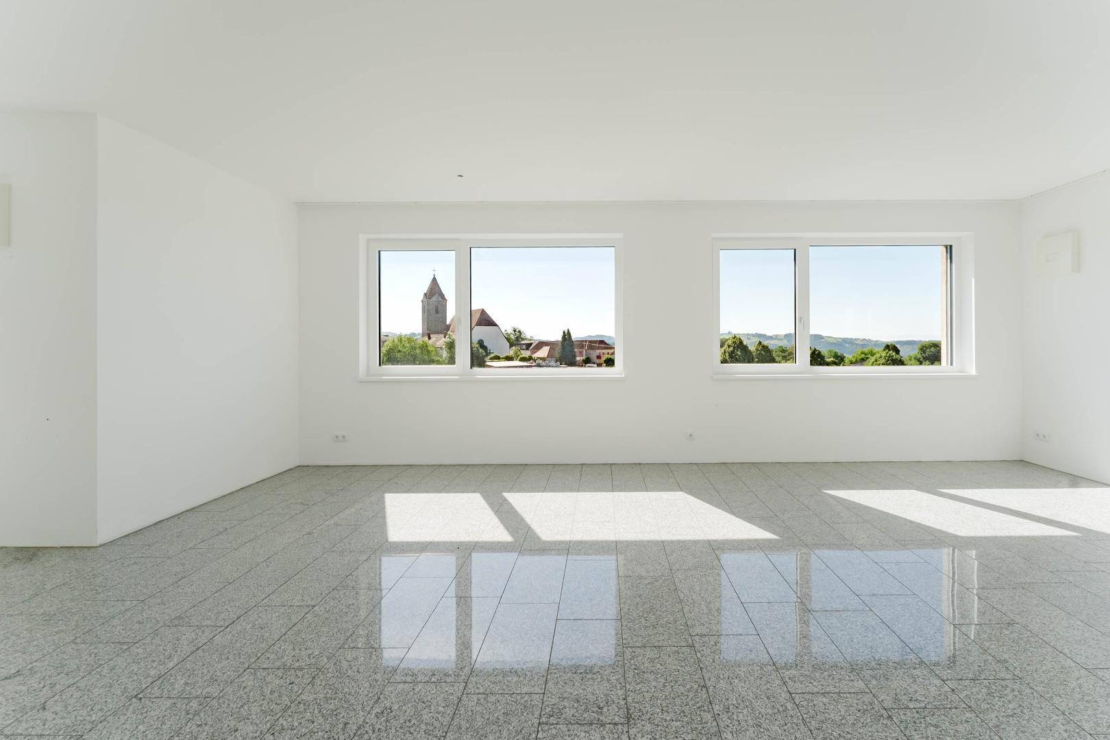 Geräumiges Zimmer mit hellen Fliesen und weitem Blick auf die umliegende Landschaft und einen Kirchturm.