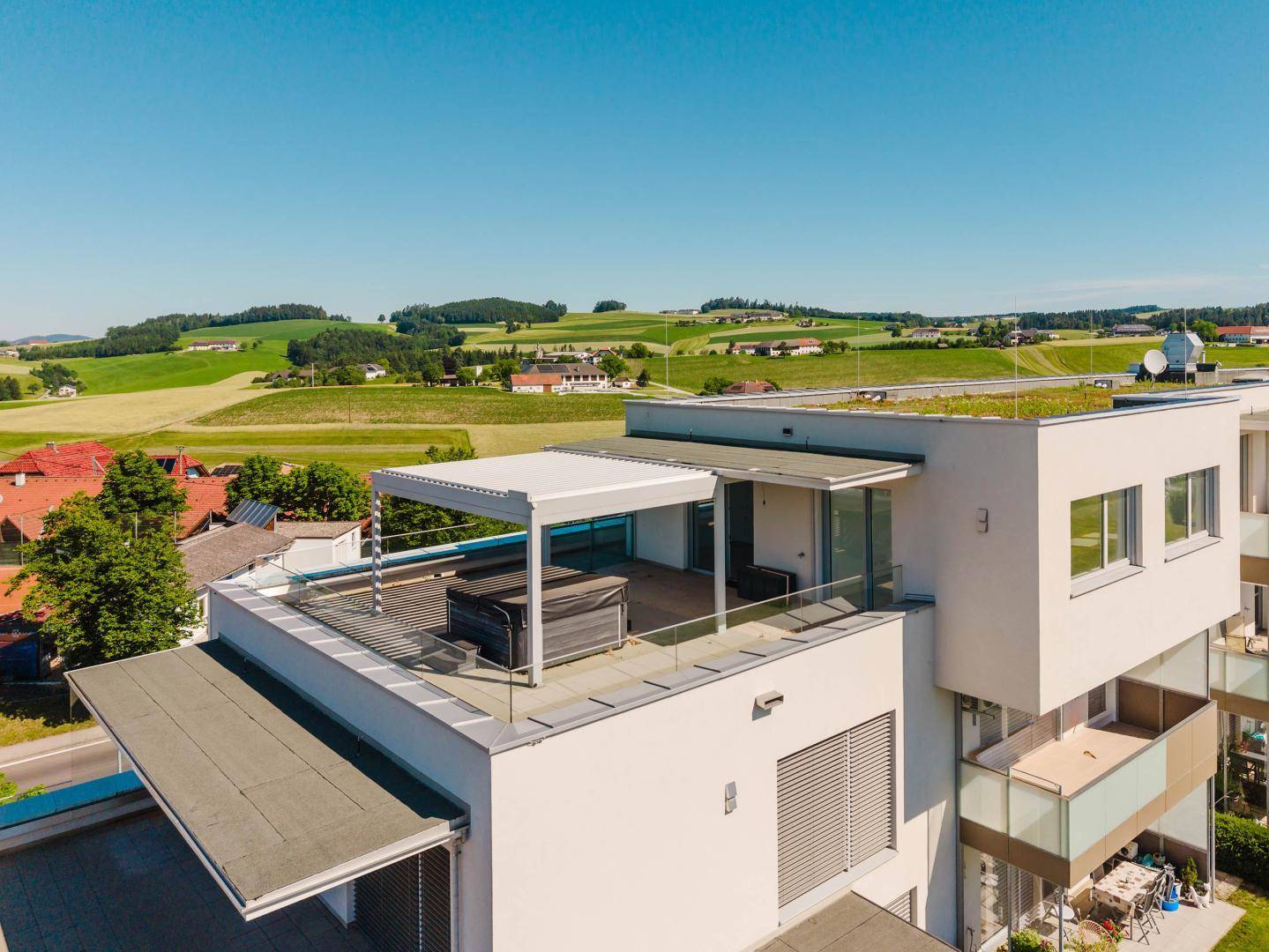 Dachterrasse mit Whirlpool und Pergola auf einem modernen Gebäude mit weitem Ausblick.