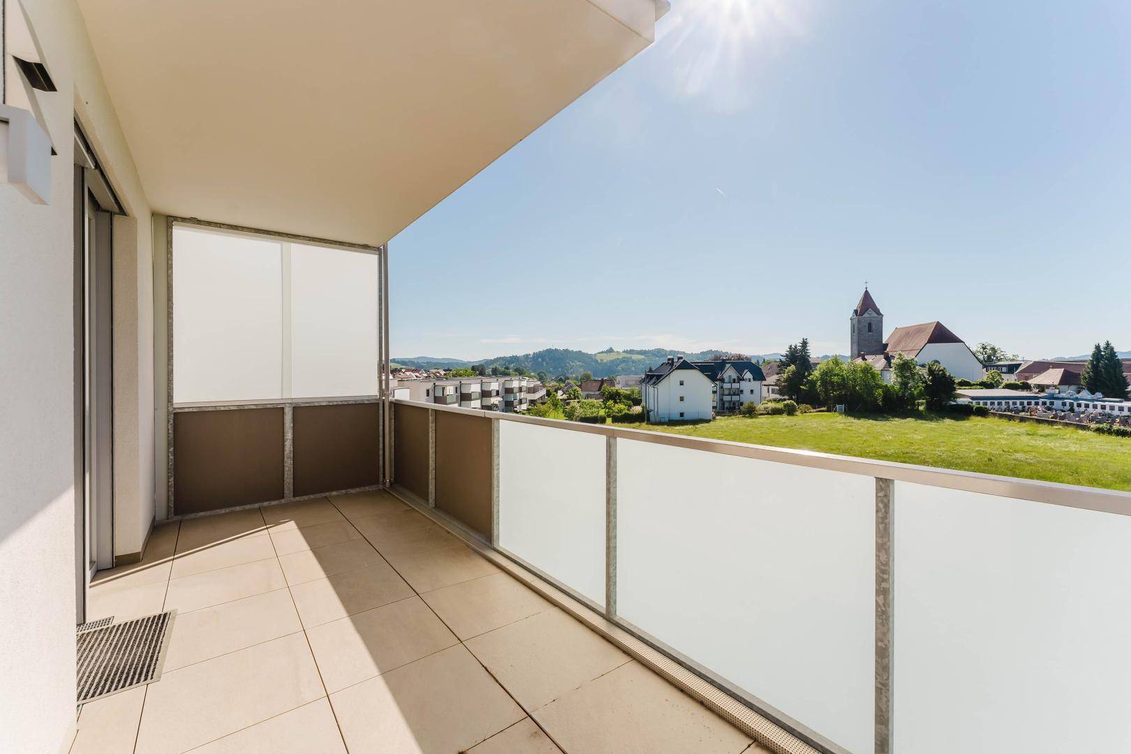 Sonniger Balkon mit Glasgeländer und Blick auf die Kirche und die Stadt.