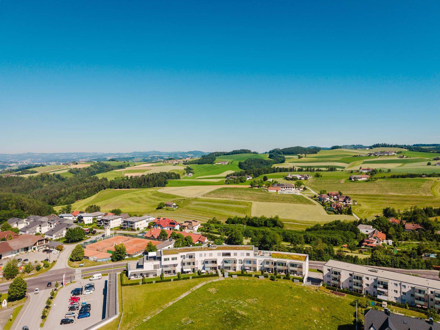Moderner Wohnkomplex mit Balkonen und Gärten, eingebettet in eine grüne Landschaft.