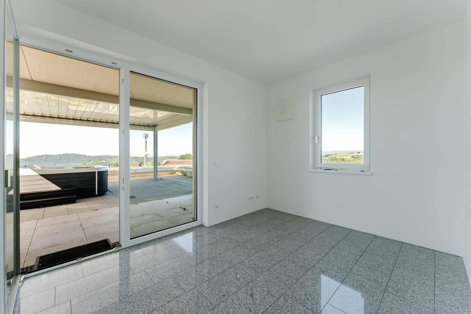 Heller Raum mit Fliesenboden und großen Schiebetüren zur Dachterrasse mit Whirlpool.