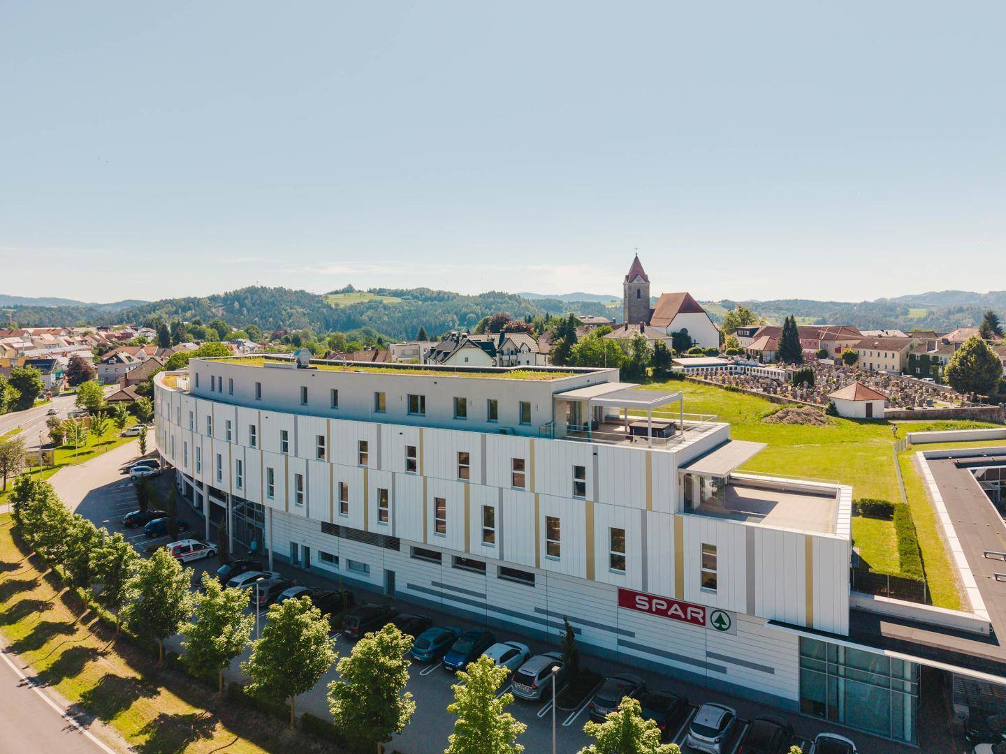 Moderne Fassade des Gebäudes mit Gründach und umliegender ländlicher Umgebung.