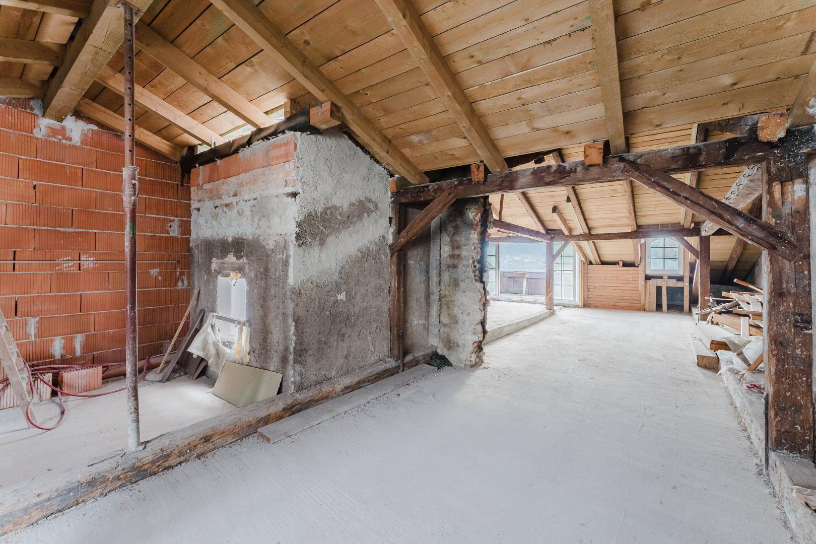 Dachboden im Rohbau mit Ziegelwänden und Holzbalken, bereit zum Ausbau.
