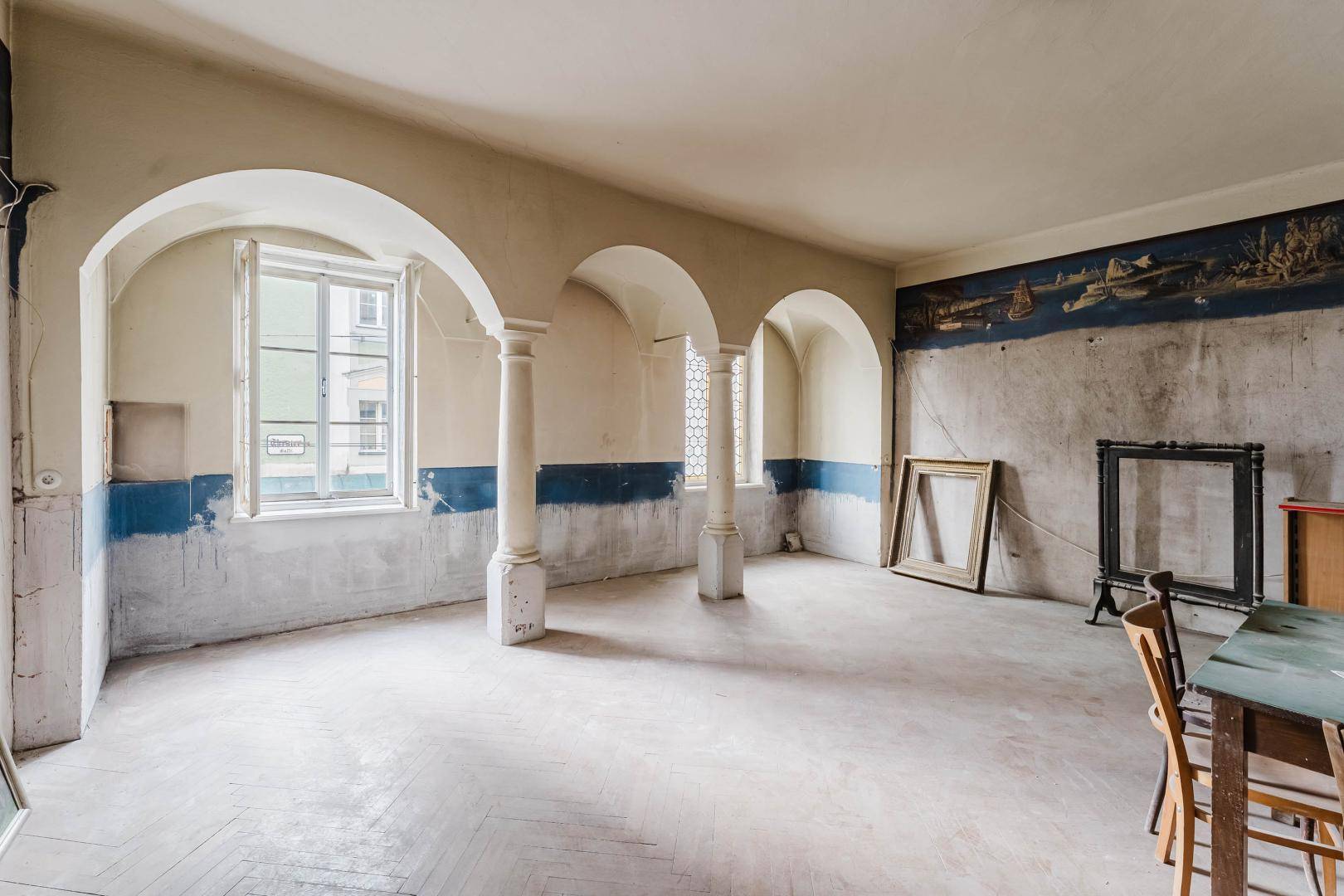 Geräumiger Raum mit Bögen, Säulen und einem Wandgemälde, teilweise möbliert.