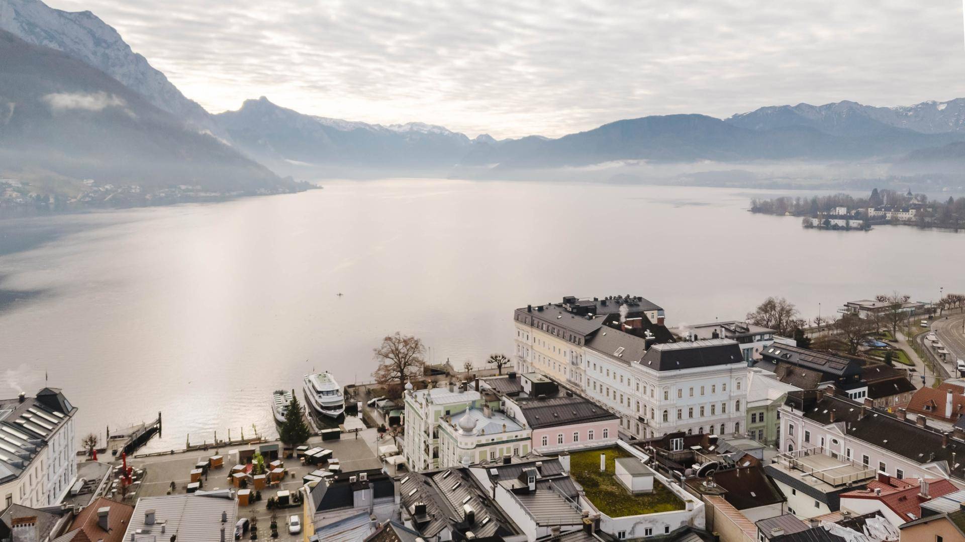 Weitläufiger Blick über den See und die Stadt mit majestätischen Bergen am Horizont.