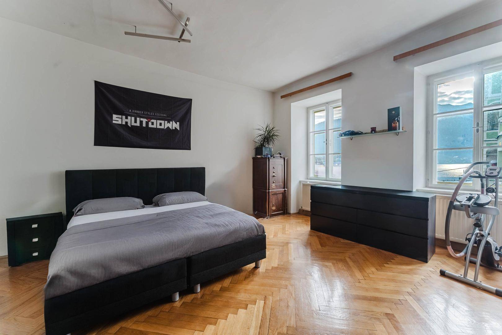 Schlafzimmer mit Parkettboden, Doppelbett und Blick auf die Berge durch die Fenster.