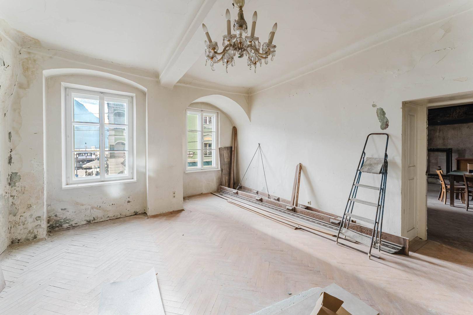 Großer Raum mit Stuckdecke, Kronleuchter und Fenstern, bereit zur Renovierung.