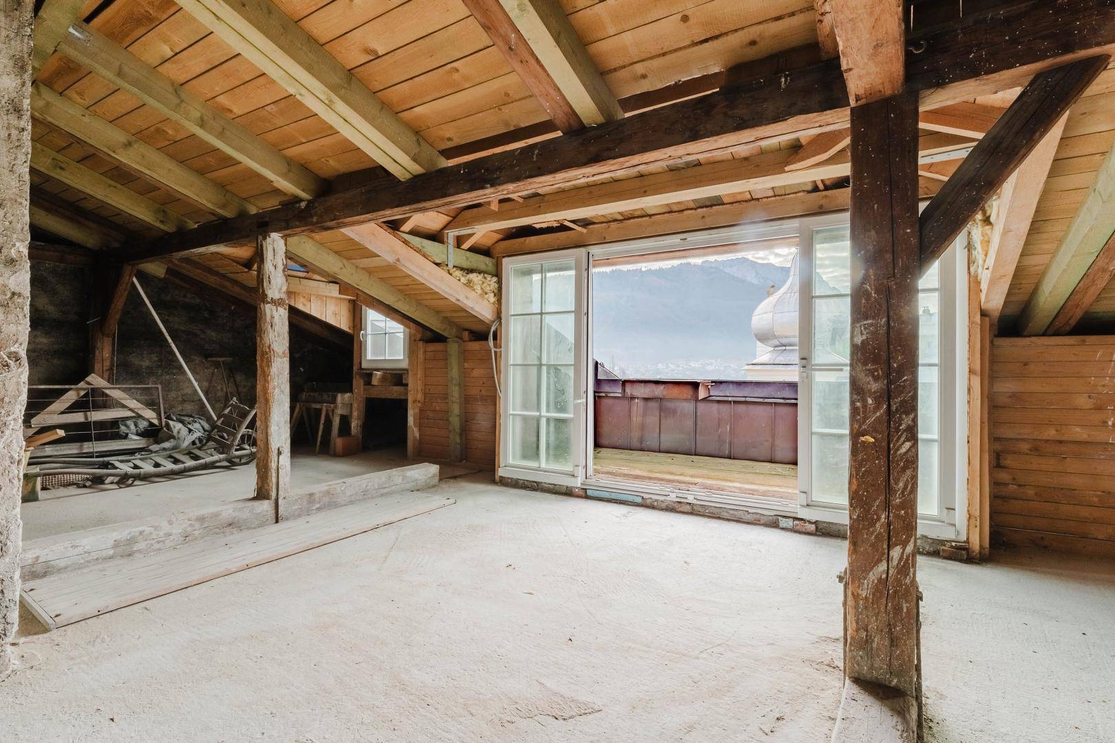Ausbaufähiger Dachboden mit sichtbaren Holzbalken und Blick auf die Berge.
