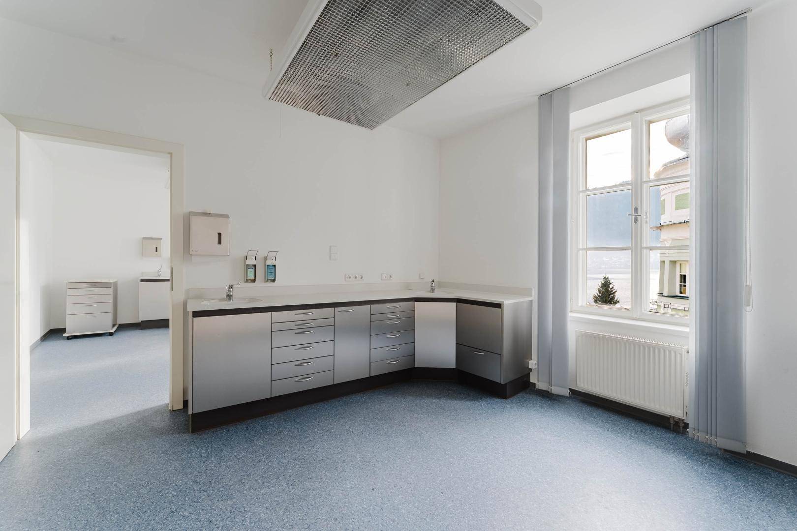 Professioneller Büroraum mit blauer Bodenfläche, Edelstahlmöbeln und großem Fenster.